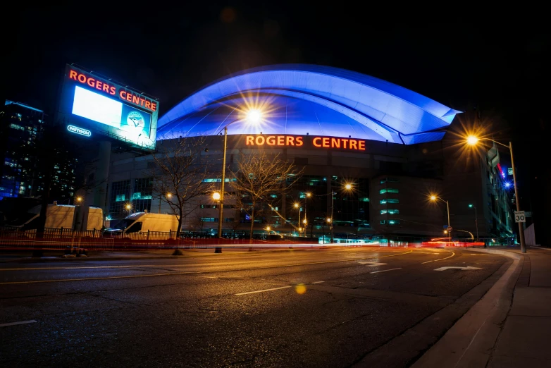 a stadium lit up with blue lights at night, a picture, by Julia Pishtar, raptors, orange roof, rob ross, exterior photo