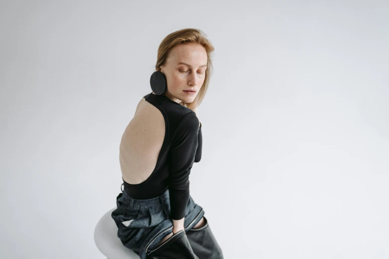 a woman sitting on top of a white chair, inspired by Anna Füssli, trending on pexels, bauhaus, left ear, black turtleneck, denim, oversized pauldrons