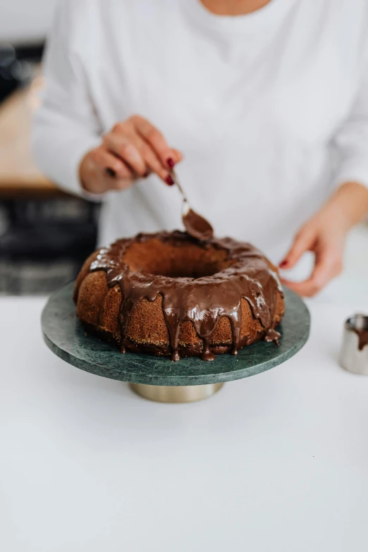 a woman is cutting into a chocolate bundt cake, a marble sculpture, pexels contest winner, in a kitchen, matte finish, product introduction photo