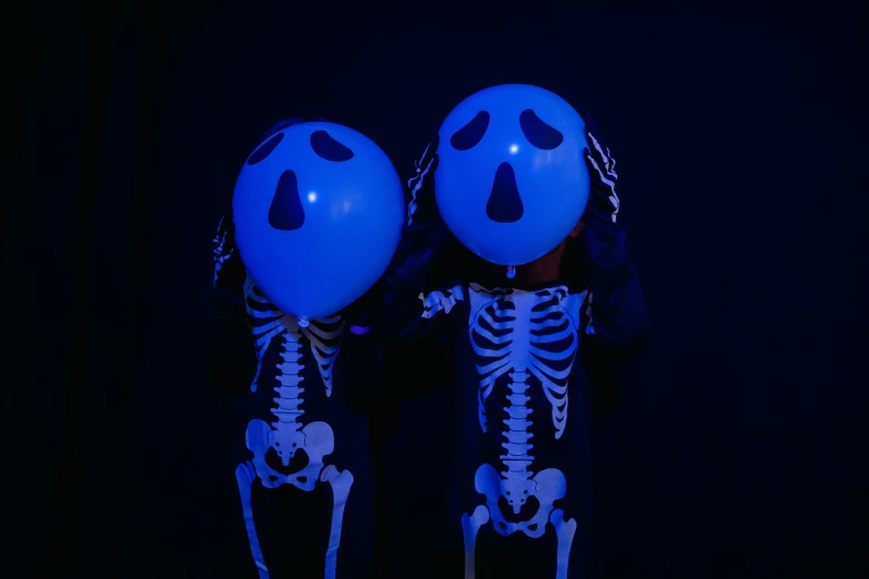 a couple of skeletons standing next to each other, by Elsa Bleda, pexels, party balloons, glowing blue face, ((blue)), twins