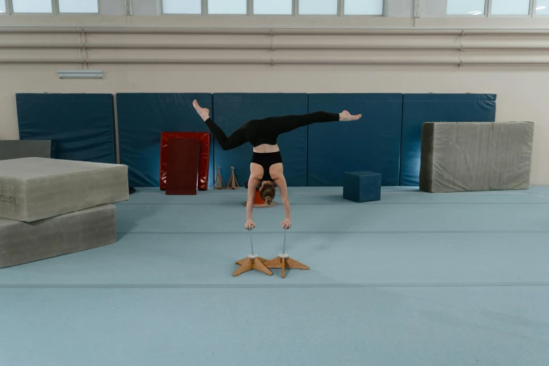 a woman doing a handstand on a gymnastics mat, inspired by Elizabeth Polunin, arabesque, cardboard, thumbnail, spider legs large, in a gym