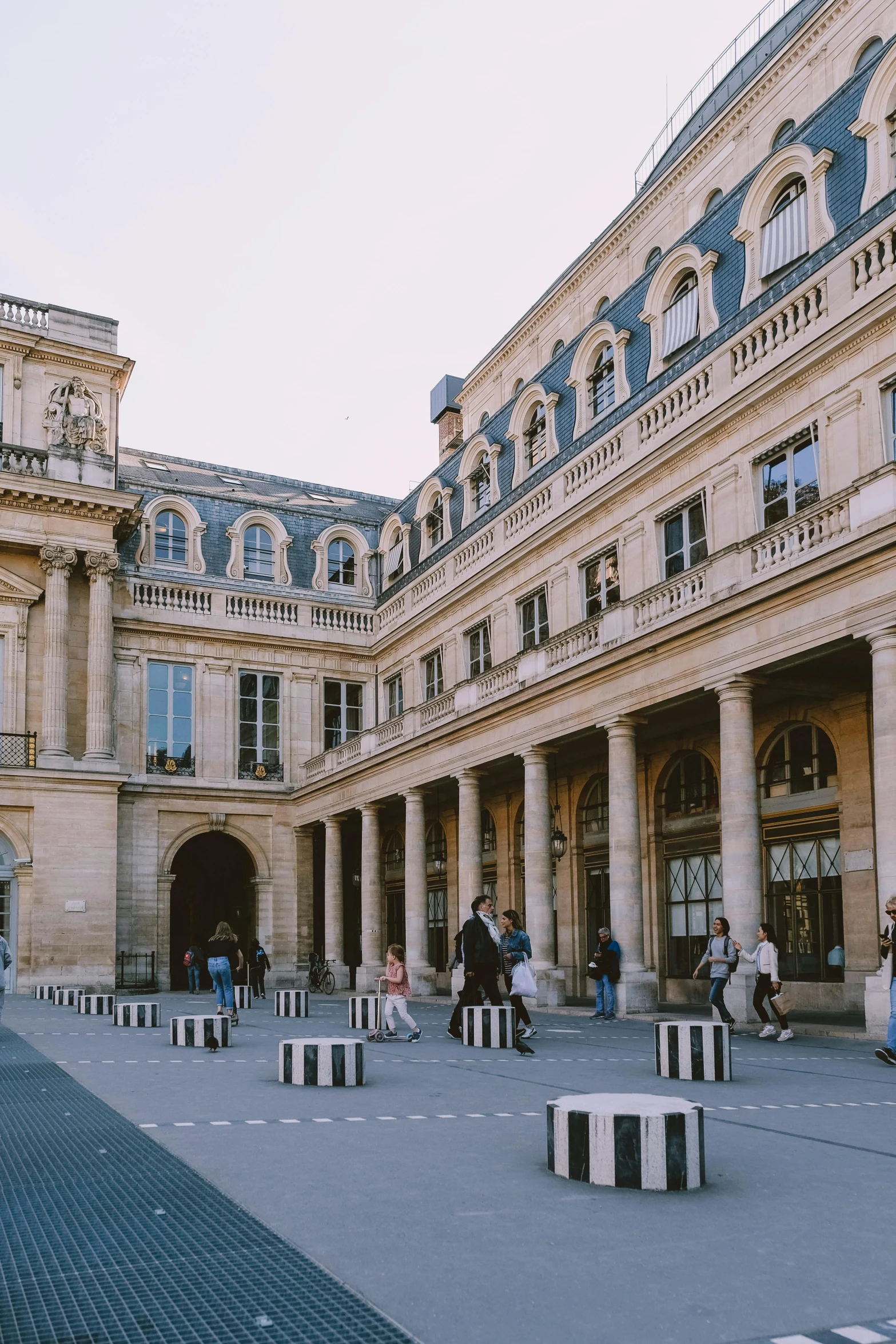 a group of people standing in front of a building, an album cover, trending on unsplash, paris school, courtyard walkway, marina abramovic, on a great neoclassical square, exterior view