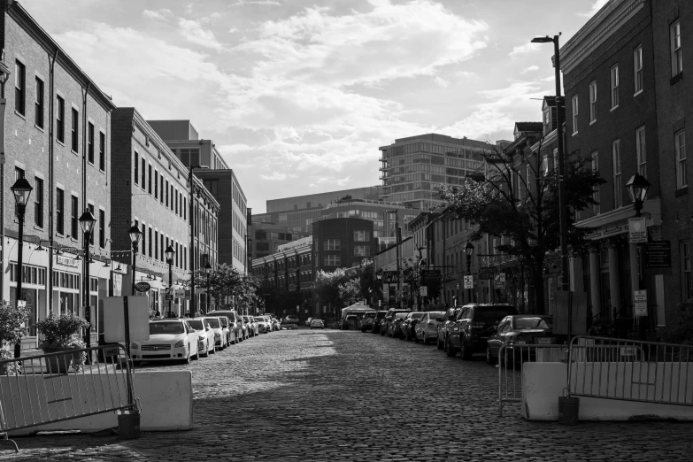 a black and white photo of a cobblestone street, by Dennis Flanders, pexels, downtown in the distance, washington dc, summer sunlight, parking in the street