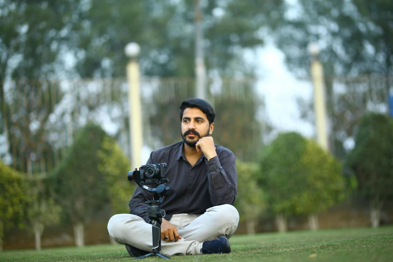 a man sitting on the ground with a camera, by Manjit Bawa, avatar image, **cinematic, realistic footage, high quality image