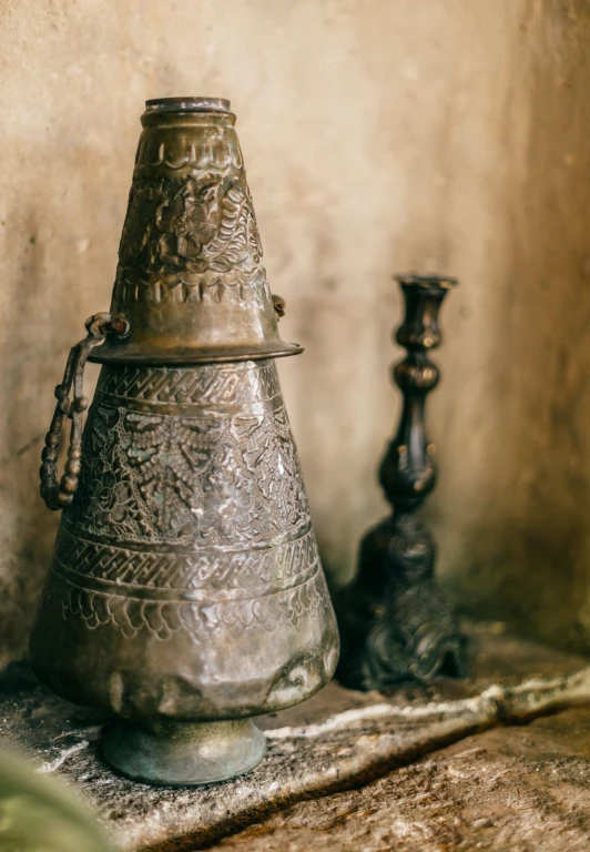 a metal vase sitting on top of a wooden table, by Adam Marczyński, trending on unsplash, folk art, moroccan mosque, bells, etched inscriptions, cone shaped