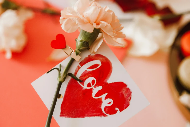 a close up of a flower with a red heart on it, on a white table, caligraphy, indi creates, place setting