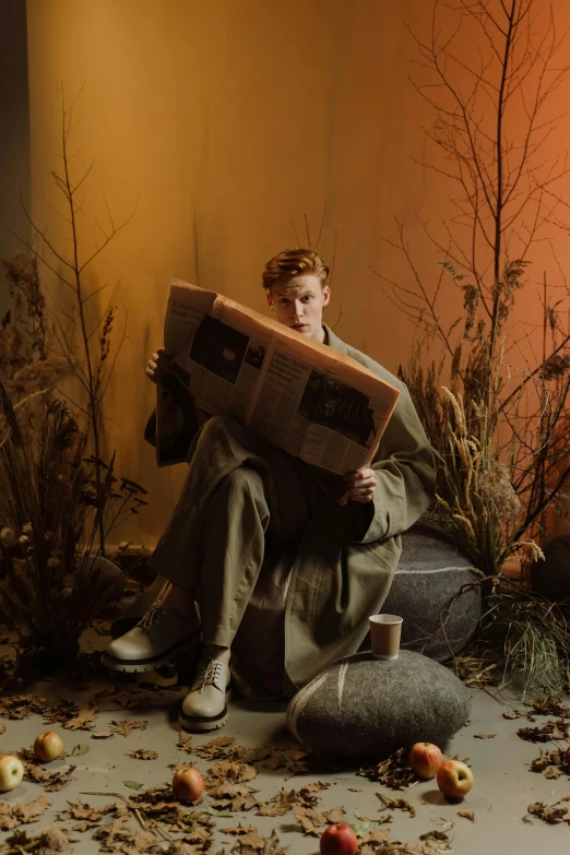 a man sitting on a rock reading a newspaper, an album cover, by Emma Andijewska, trending on pexels, magic realism, red haired teen boy, tilda swinton, hunting, studio photo