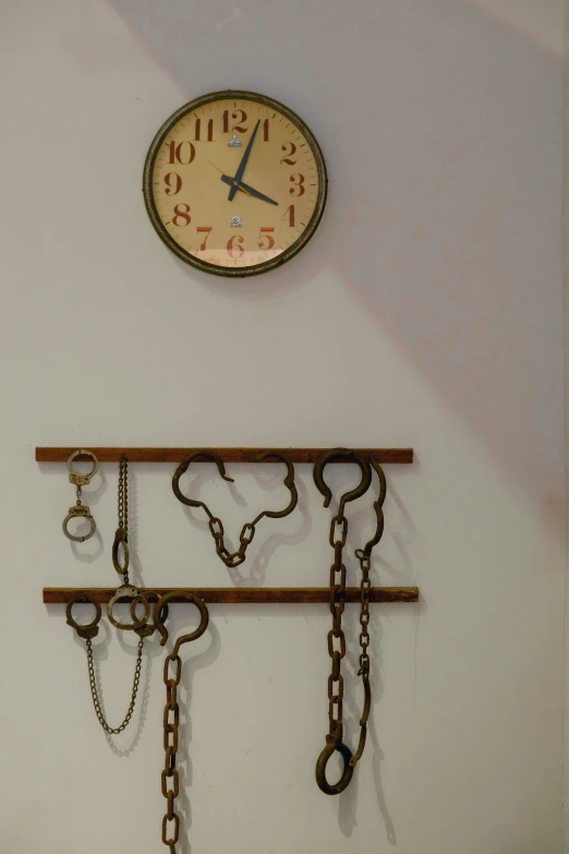 a clock hanging on a wall with chains attached to it, kinetic art, minimal artifacts, quirky shops, soviet interior, handcuffs