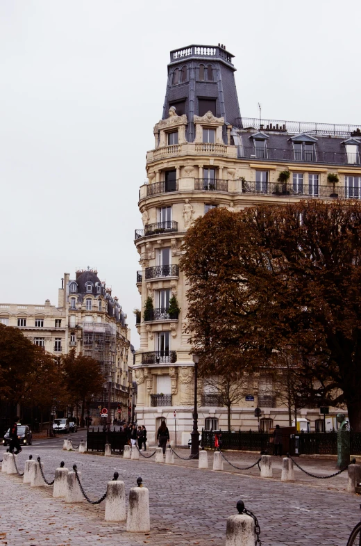 a man riding a bike down a cobblestone street, a photo, trending on unsplash, paris school, city buildings on top of trees, rounded architecture, late autumn, overcast day