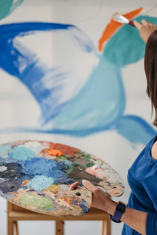 a woman in a blue dress painting on a canvas, trending on unsplash, arbeitsrat für kunst, multicoloured, looking from shoulder, professional image, shades of blue and grey