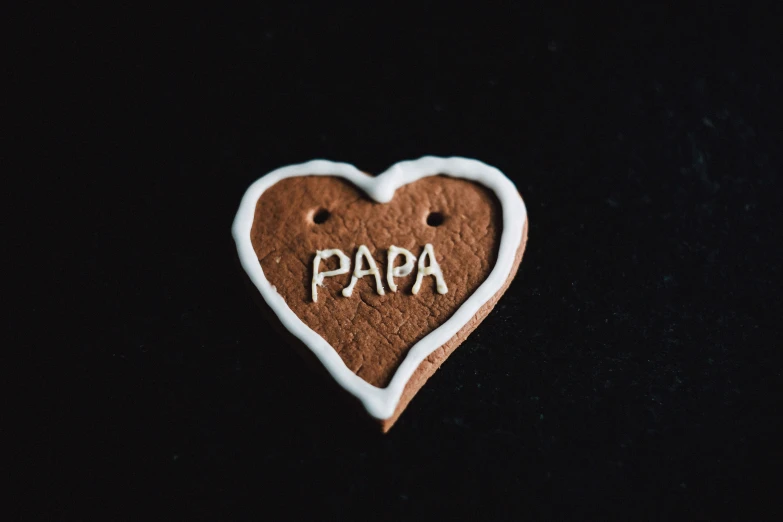 a heart shaped cookie with the word papa written on it, pexels, dada, with a black background, avatar image, clay amulets, grandfatherly