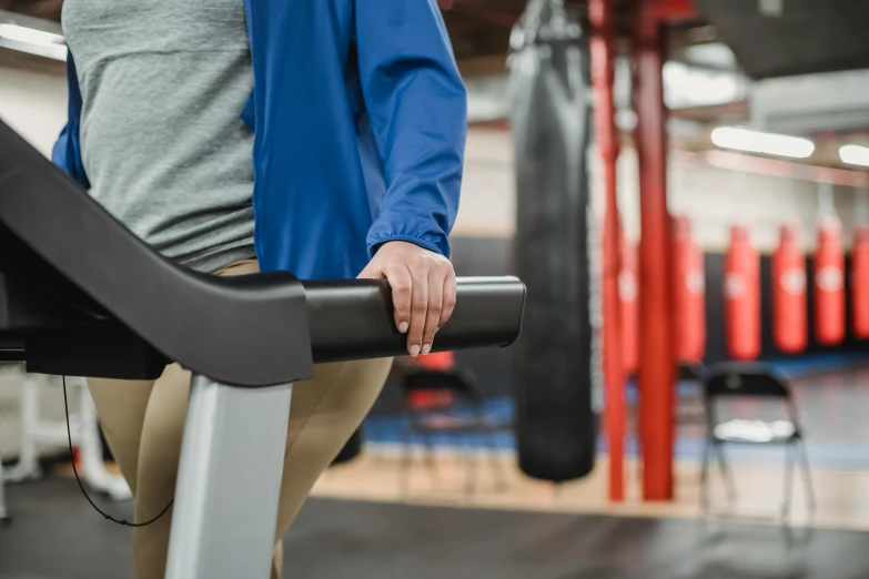 a woman standing on a tread machine in a gym, trending on pexels, no - text no - logo, background image, conor walton, holding a staff