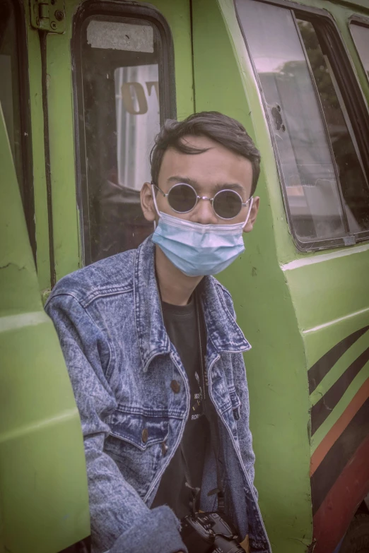 a man wearing a face mask in front of a bus, trending on pexels, sumatraism, androgynous person, wearing shades, avatar image, julian ope
