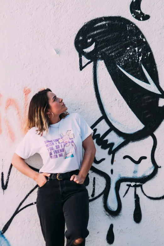 a woman standing in front of a wall with graffiti, a cartoon, by Mór Than, trending on unsplash, white t-shirt, violet coloured t-shirt, 90s photo, plain walls |light hearted