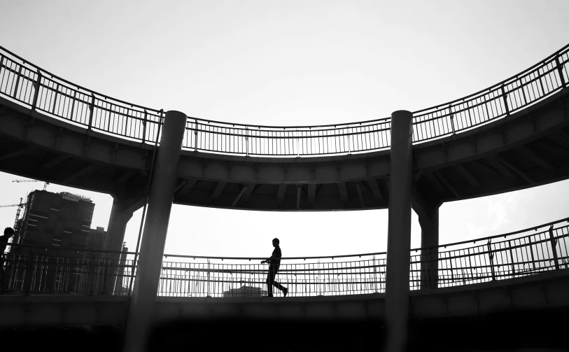 a black and white photo of a person walking on a bridge, inspired by Cheng Jiasui, rounded architecture, silhouette of a man, running, monochrome color