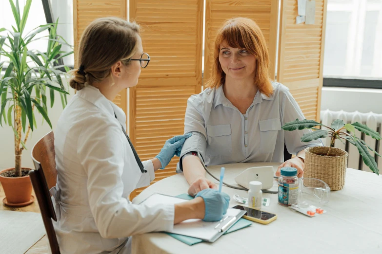 two women sitting at a table talking to each other, a photo, by Adam Marczyński, pexels, renaissance, with an iv drip, doctors office, background image