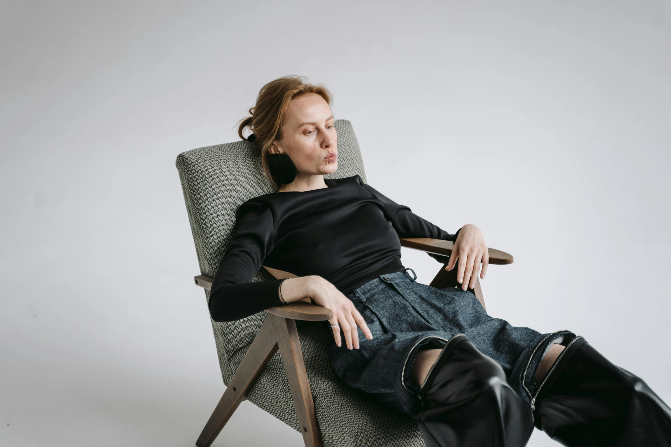 a woman sitting in a chair with her legs crossed, inspired by Sarah Lucas, trending on pexels, sleepy fashion model face, jeans and black boots, humanoid woman, alexey gurylev