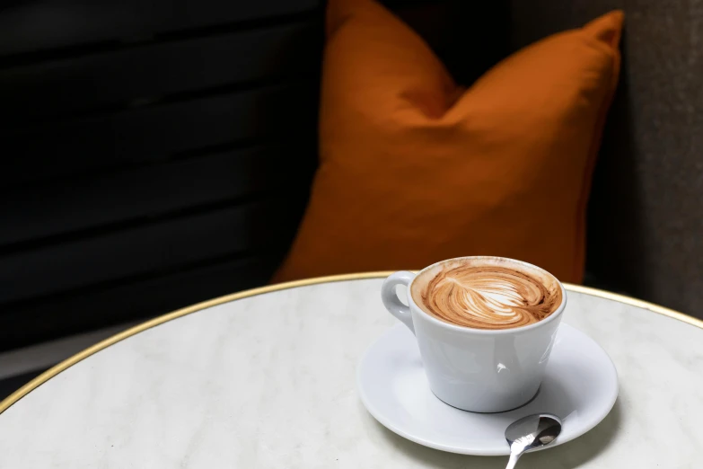 a cup of coffee sitting on top of a white table, inspired by Charles Le Roux, private press, lounge, ochre, over the shoulder, thumbnail