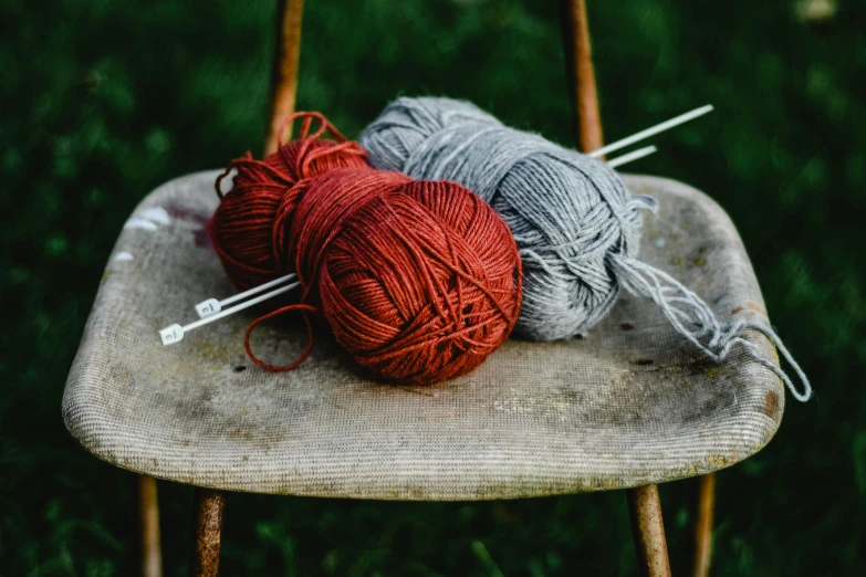 two balls of yarn sitting on top of a wooden chair, a portrait, unsplash, red and grey only, gardening, grey, exterior shot