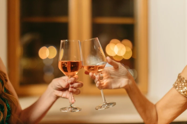 two women toasting with wine glasses in front of a window, by Carey Morris, pexels contest winner, light pink tonalities, it's night, hands in air, understated