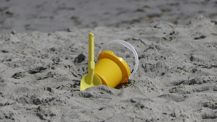 a yellow bucket sitting on top of a sandy beach, playing, grey, small, hansa yellow