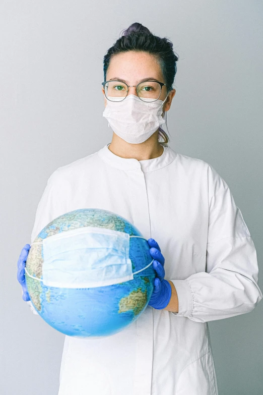 a woman in a white lab coat holding a globe, face mask, thumbnail, traveller, synthetic materials