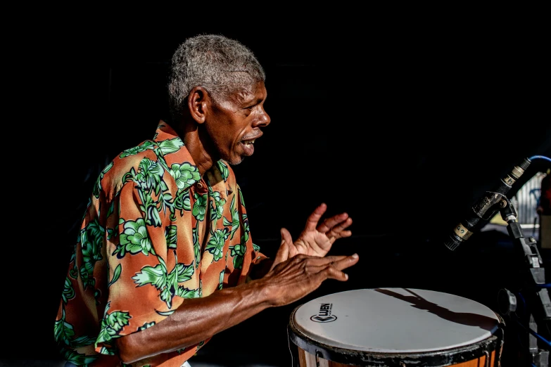 a man standing next to a drum on a stage, pexels contest winner, black arts movement, cuba, thumbnail, old man, 15081959 21121991 01012000 4k