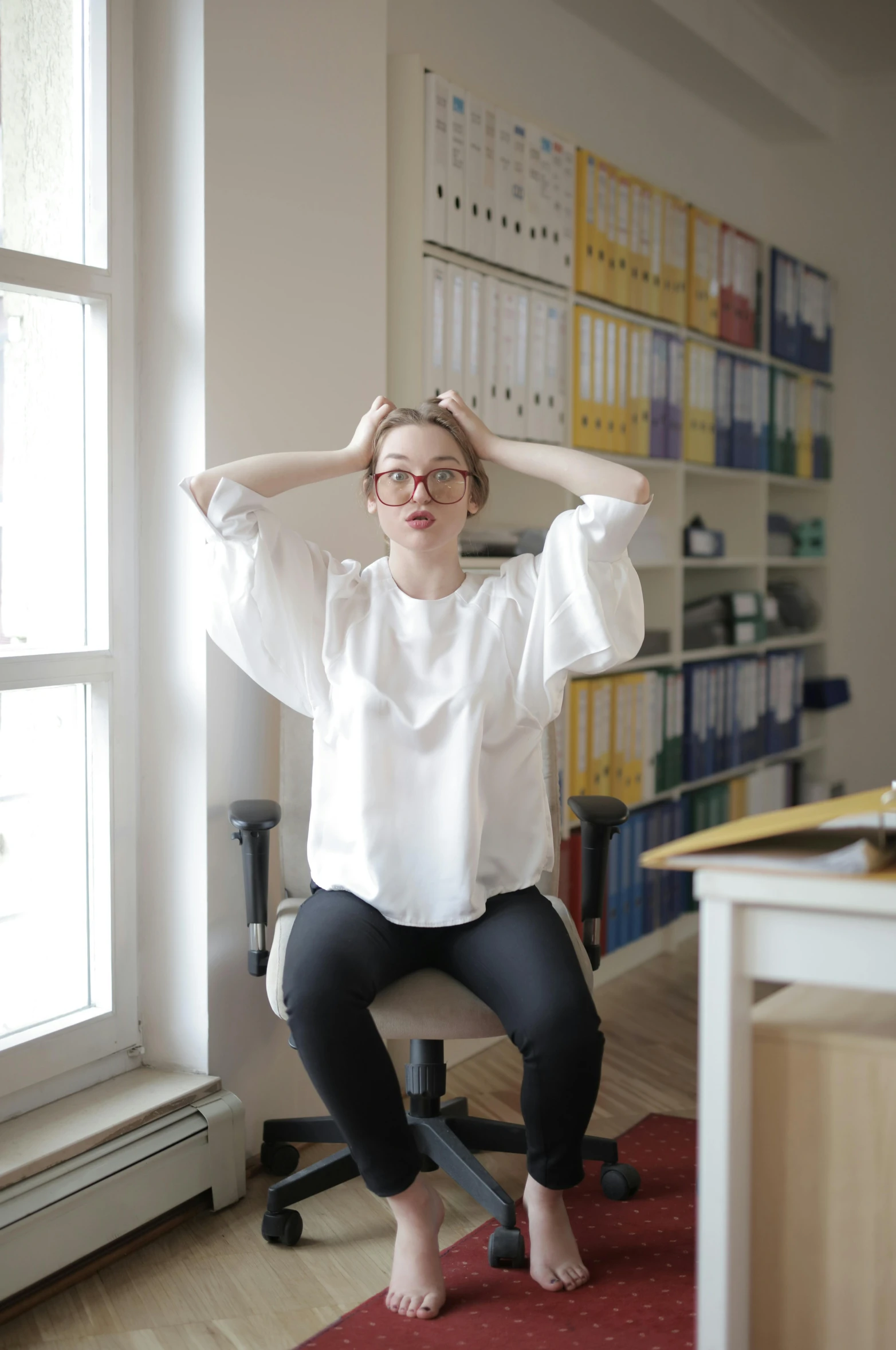 a woman sitting on a chair in front of a window, frustrated, wearing a light shirt, dynamic energic pose, librarian