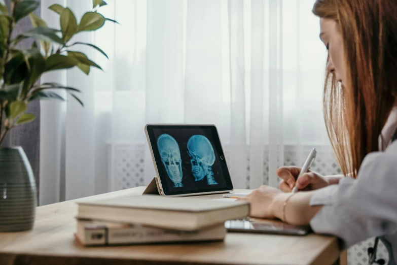 a woman sitting at a table in front of a laptop computer, a hologram, by Julia Pishtar, unsplash, medical dissection, took on ipad, a wooden, aged 13