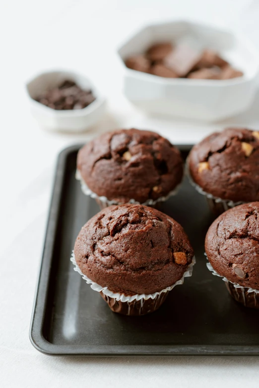 a tray of chocolate muffins sitting on top of a table, by Everett Warner, unsplash, square, panorama, kek, lulu chen