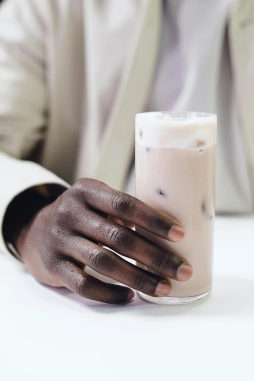 a man sitting at a table with a glass of milk, by Lily Delissa Joseph, trending on unsplash, photorealism, unmistakably kenyan, holding hand, white with chocolate brown spots, made of smooth black goo