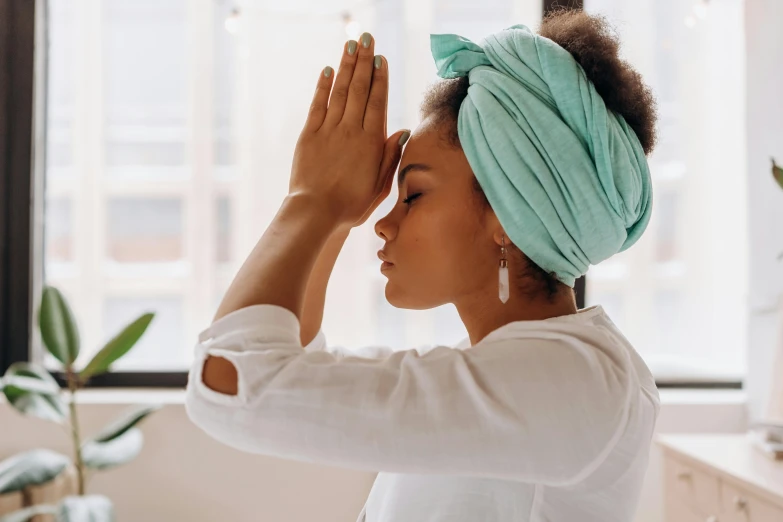 a woman in a turban standing in front of a window, trending on pexels, hurufiyya, channeling third eye energy, paws on head, teal headband, doing a prayer