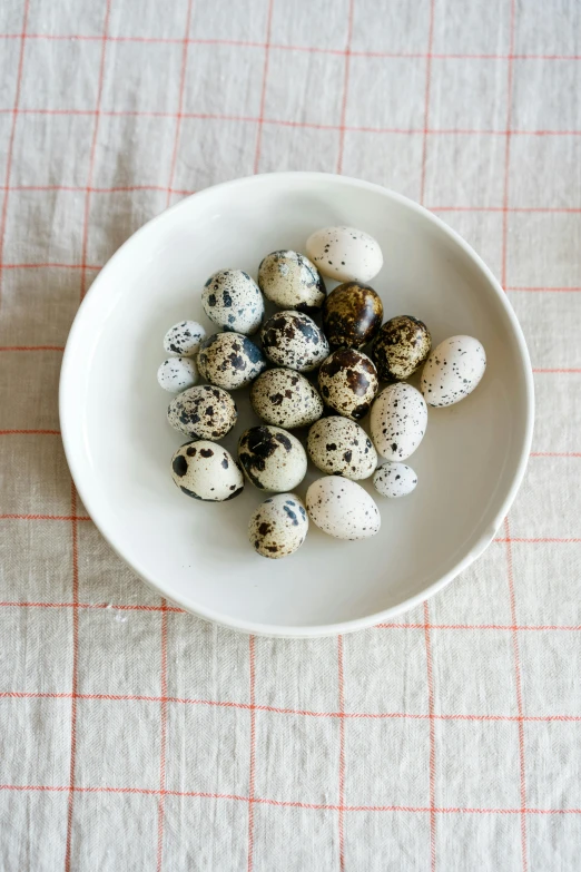 a white bowl filled with eggs on top of a table, by Jessie Algie, unsplash, white with black spots, dragon eggs, square, dwell