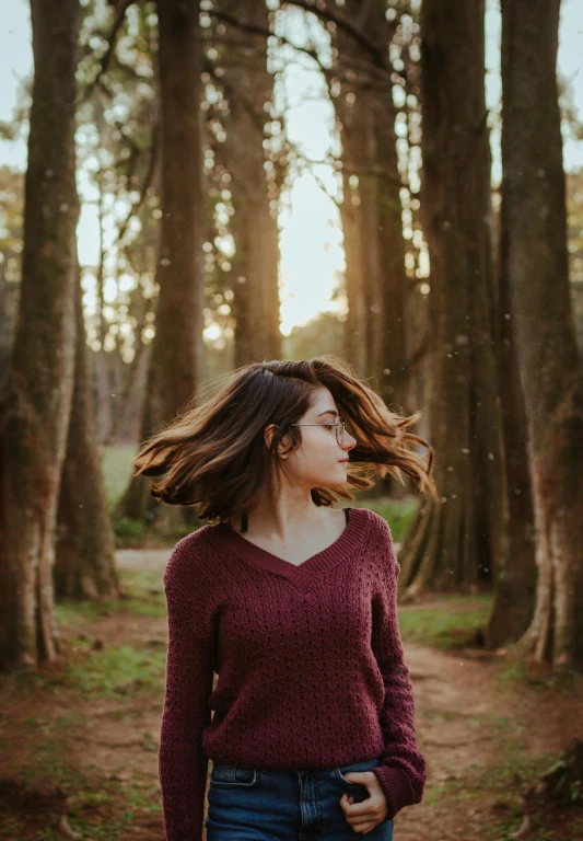 a woman standing in the middle of a forest, pexels contest winner, wavy hair combed to one side, wearing casual sweater, profile pic, swaying trees