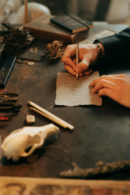 a person sitting at a table writing on a piece of paper, a still life, trending on unsplash, arts and crafts movement, jewelry made of bones, weta workshop, using leather armour with bones, professional gunsmithing