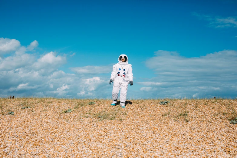 a man in a white space suit standing in a field, inspired by Storm Thorgerson, unsplash, at the seaside, lunar themed attire, blue skies, small astronauts