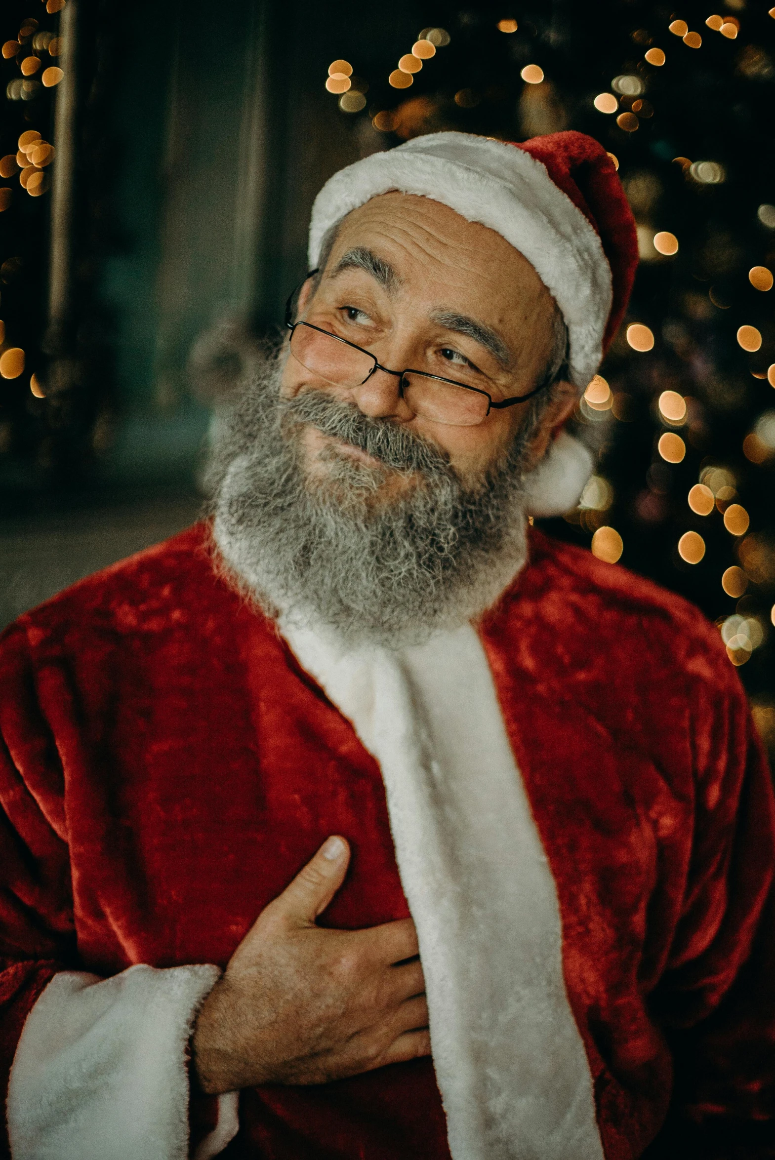 a man dressed as santa claus standing in front of a christmas tree, a photo, pexels, photorealism, big smirk, bl