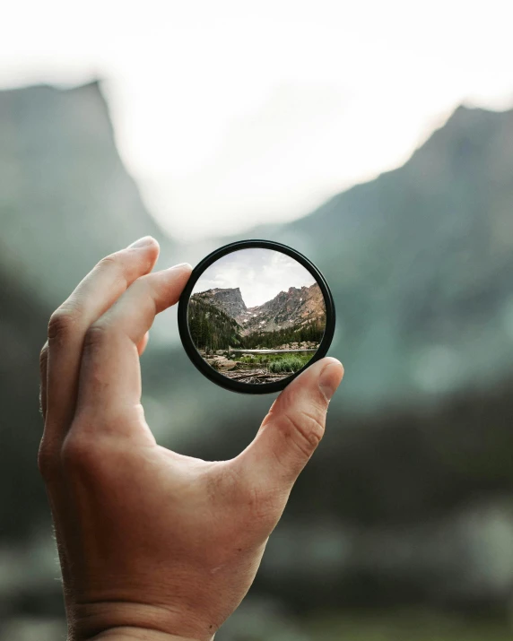 a person holding a circular object with mountains in the background, a picture, unsplash contest winner, round windows, zoom lens, offering the viewer a pill, mirrors