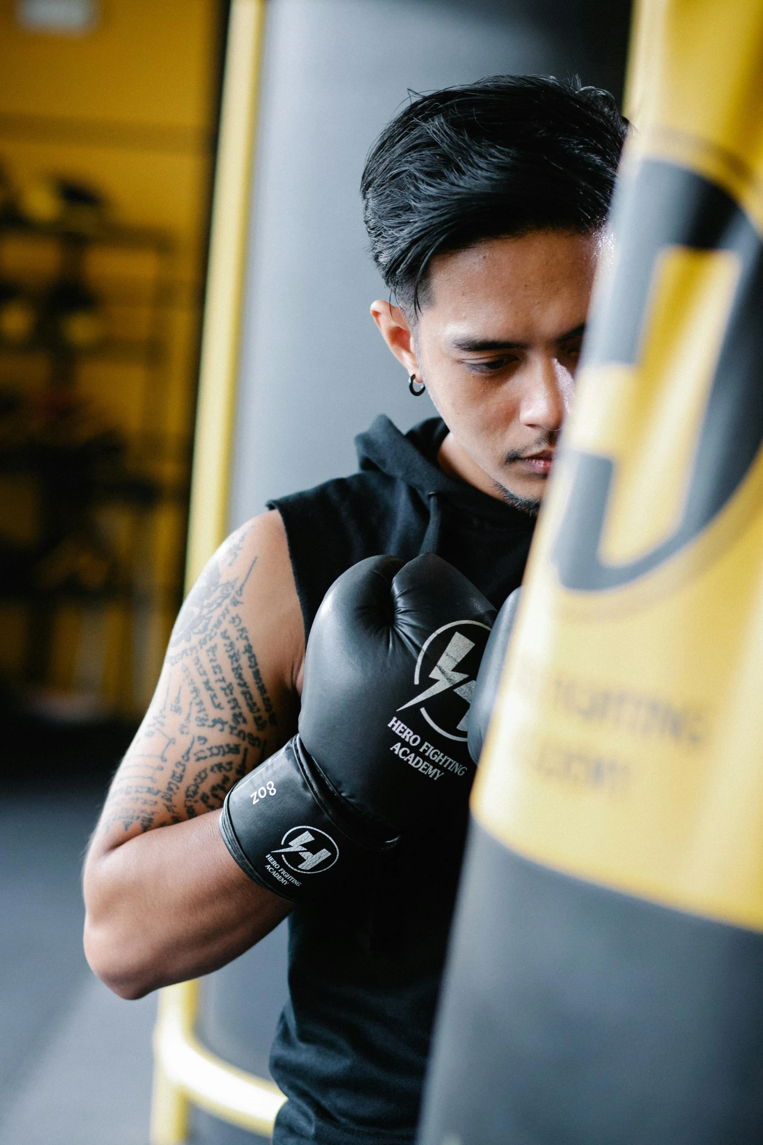 a man standing next to a punching bag, by Robbie Trevino, hurufiyya, black and yellow tracksuit, fist training, thumbnail, manuka