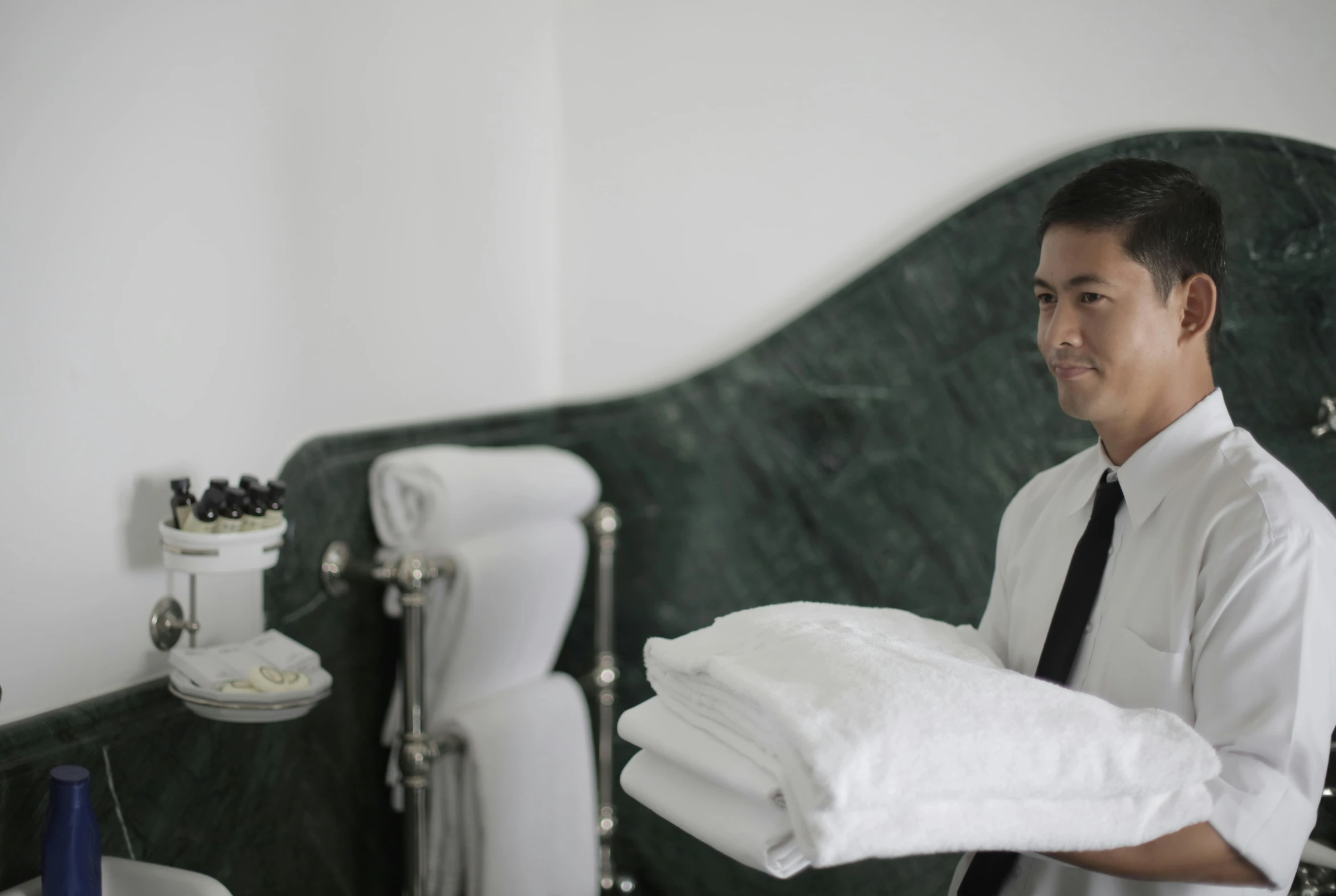 a man holding a pile of towels in a bathroom, a portrait, unsplash, marble room, maid, profile image, thawan duchanee