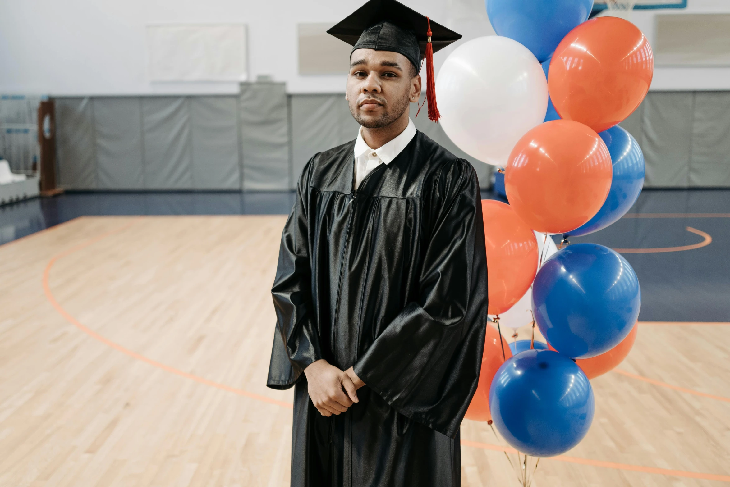 a man standing in front of a bunch of balloons, unsplash, academic art, wearing an academic gown, in the high school gym, black man, a handsome