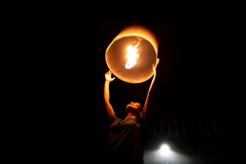 a man holding a light up in the dark, an album cover, by Gina Pellón, pexels contest winner, barrel fires and tents, laos, a woman holding an orb, fire above head