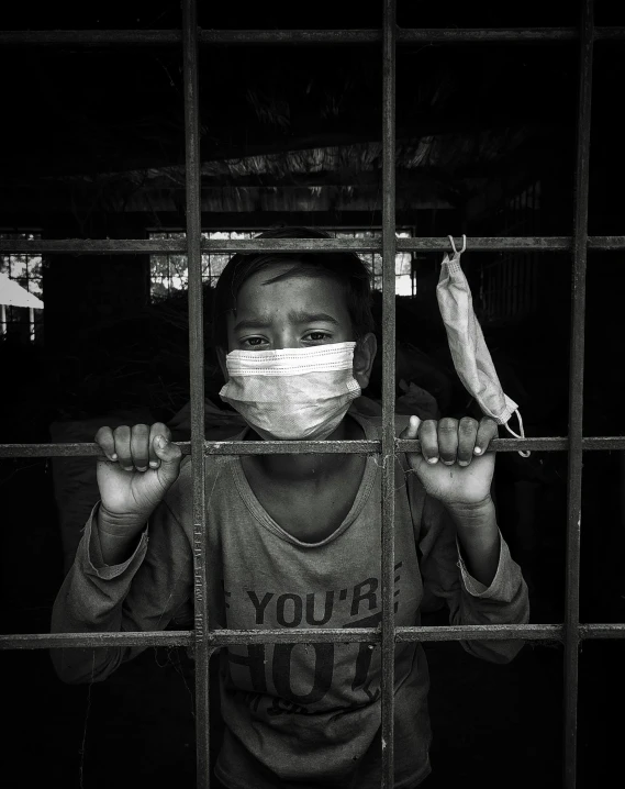 a black and white photo of a boy wearing a face mask, stood in a cell, myanmar, ariel perez, clean borders