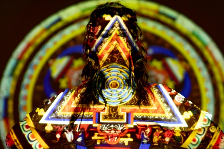 a man that is standing in front of a light, inspired by Harry Clarke, psychedelic art, aztec iconography, projection mapping, yantra, she is dressed in shaman clothes