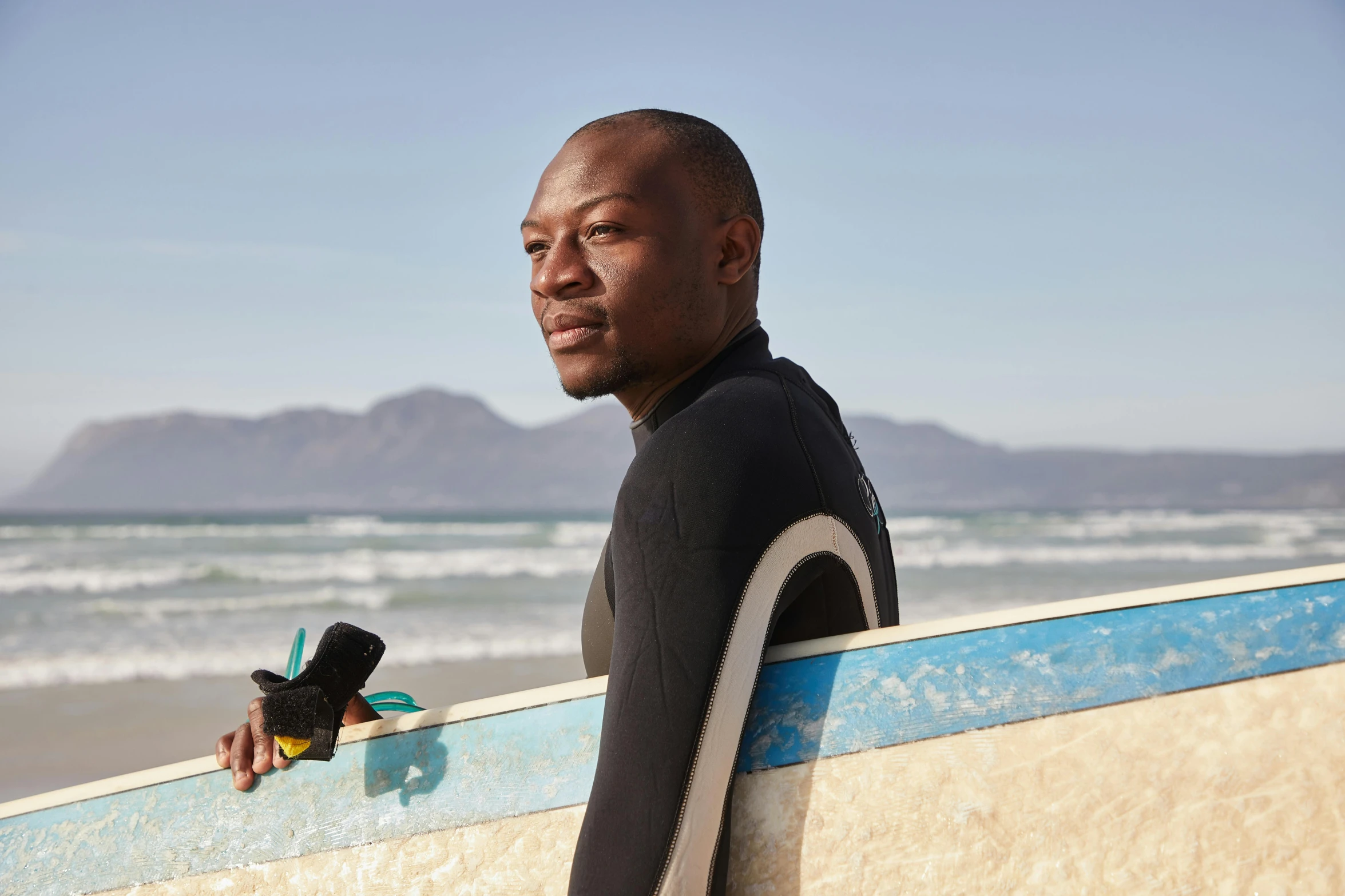 a man standing on a beach holding a surfboard, inspired by Barthélemy Menn, happening, profile image, man is with black skin, professional profile photo, looking towards camera