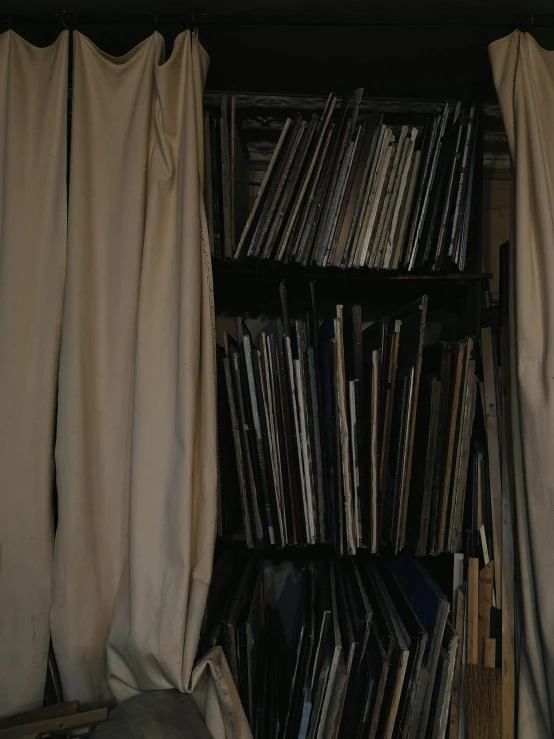 a bookshelf filled with lots of books next to a window, an album cover, unsplash, tonalism, fully covered in drapes, archive material, medium closeup, in his basement studio