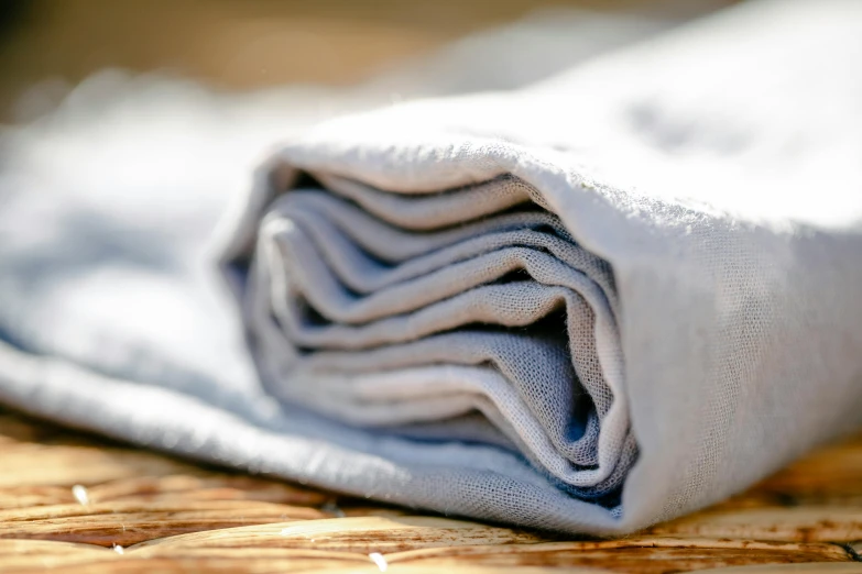 a stack of folded towels sitting on top of a wooden table, by Helen Stevenson, unsplash, soft grey and blue natural light, detail shot, moonlight grey, made of glazed