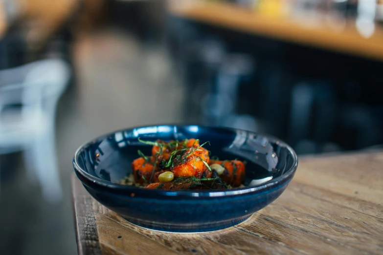 a bowl of food sitting on top of a wooden table, unsplash, dipped in polished blue ceramic, square, with seaweed, stew