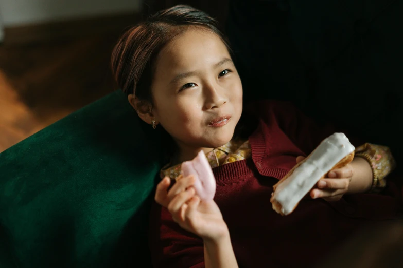 a little girl sitting on a couch eating a donut, pexels contest winner, chinese heritage, a plaster on her cheek, holding a baguette, chewing on a video card