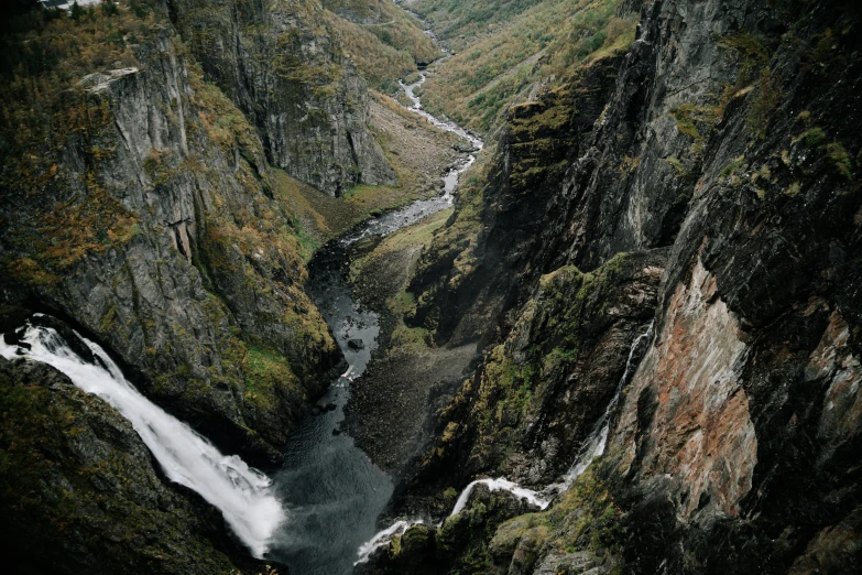 a man standing on top of a cliff next to a waterfall, by Jesper Knudsen, pexels contest winner, hurufiyya, wide high angle view, thumbnail, small river, in between a gorge